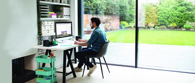 Un employé travaille depuis son bureau à domicile. Il est assis à un bureau et travaille sur un ordinateur de bureau avec une imprimante d'étiquette Brother P-touch à ses côtés pour contribuer à renforcer la productivité de l'entreprise.