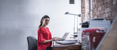 Une femme assise à son bureau utilise un ordinateur portable. Devant elle se trouve une imprimante Brother.