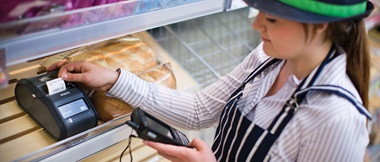 Une jeune femme travaillant pour un commerce alimentaire imprime une étiquette à l'aide d'une imprimante d'étiquettes portable de marque Brother
