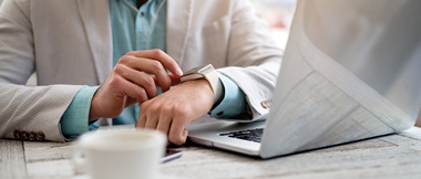 Un homme assis près de son ordinateur portable consulte sa montre connectée.