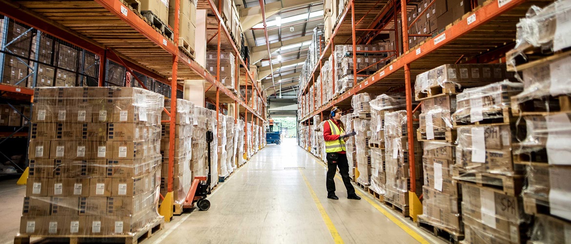 Une employée d'un entrepôt ou d'un centre de distribution tient, dans ses mains, un presse-papier à côté des boîtes, des rayonnages orange