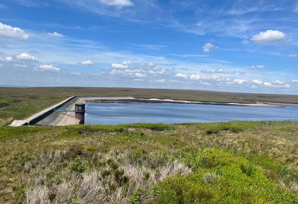 Réservoir de Dovestone rempli d'eau au milieu d'une herbe verte et d'un ciel bleu parsemé de nuages